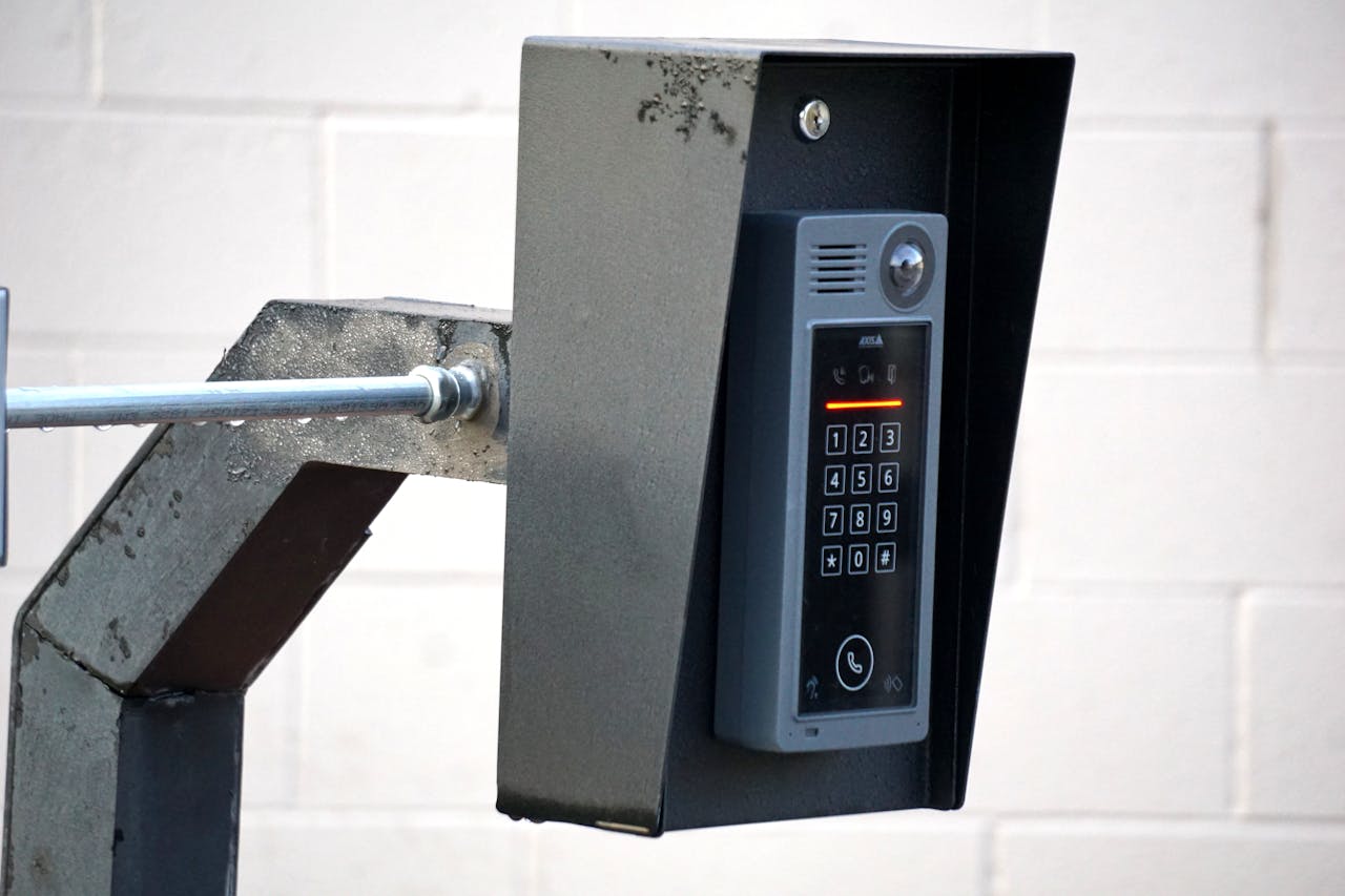 Close-up of a modern security intercom and keypad mounted on a wall outdoors with visible wiring.